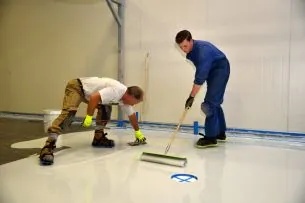 Zwei Handwerker tragen eine Bodenbeschichtung auf
